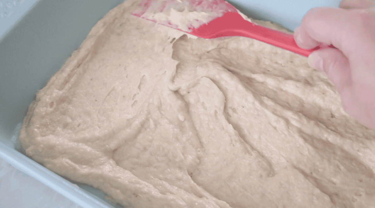 Spatula spreading banana bread batter into pan.