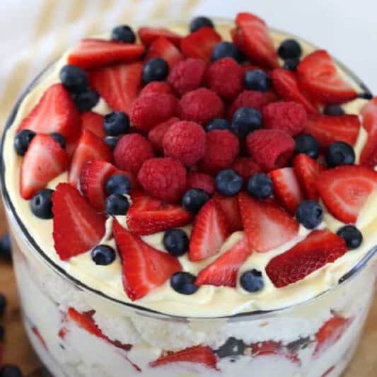 trifle bowl layered with whipped cream, squares of angel food cake and strawberries, raspberries and blueberries