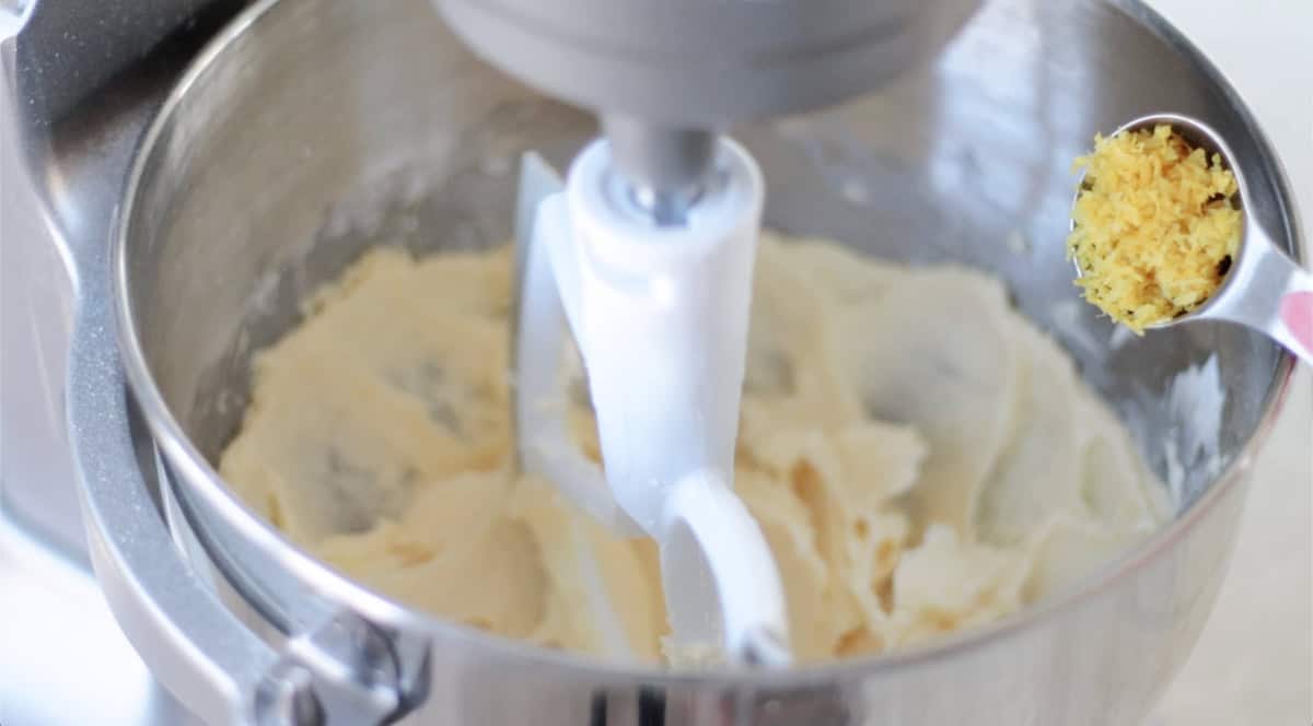 Stand mixer with cookie dough and spoonful of lemon zest being added to it.