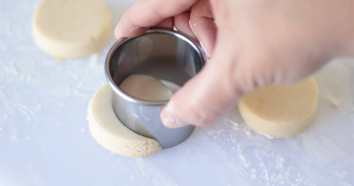 Hand pressing circle cookie cutter into cookie dough to make a crescent shape.