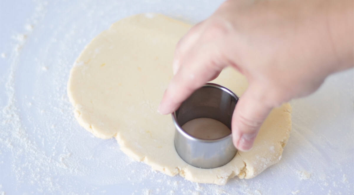 Hand pressing cookie cutter into cookie dough.