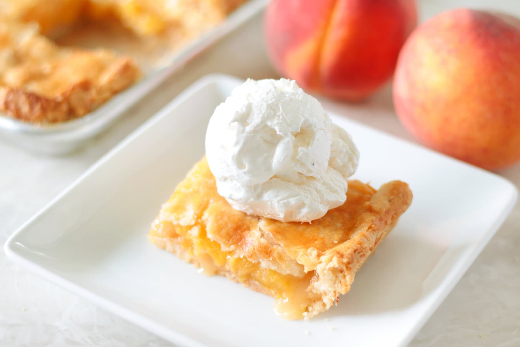 slice of peach slab pie on plate with scoop of vanilla ice cream on top