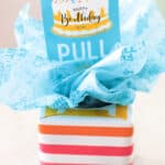 Tissue box wrapped in gift wrap and tissue paper with a pull tag.