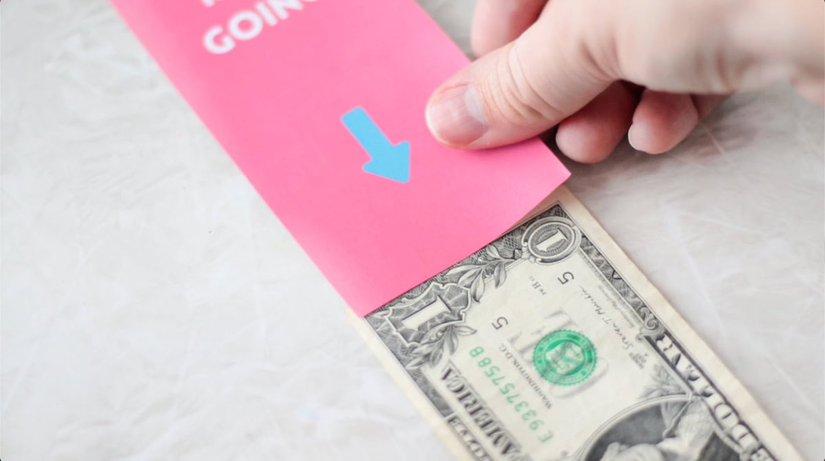 Hand placing printable tag on dollar bill.