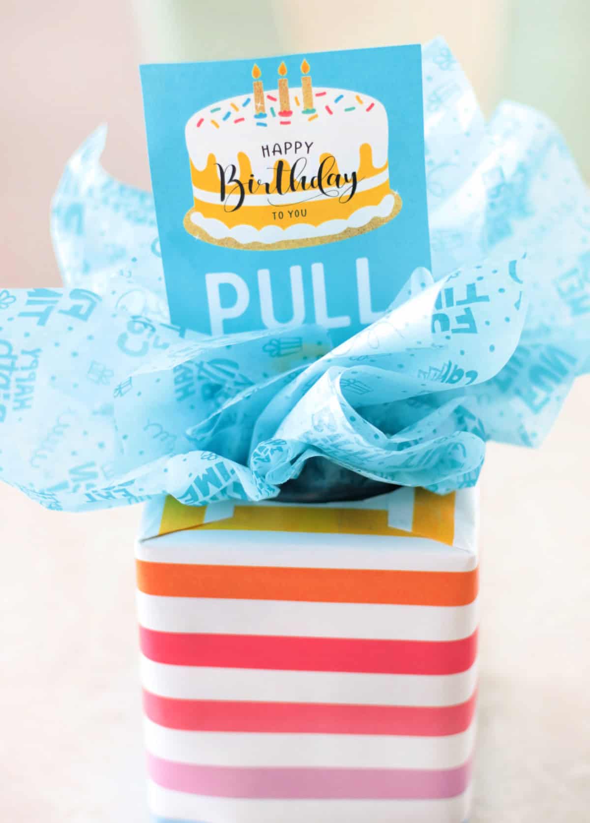 Tissue box wrapped in gift wrap and tissue paper with a pull tag.