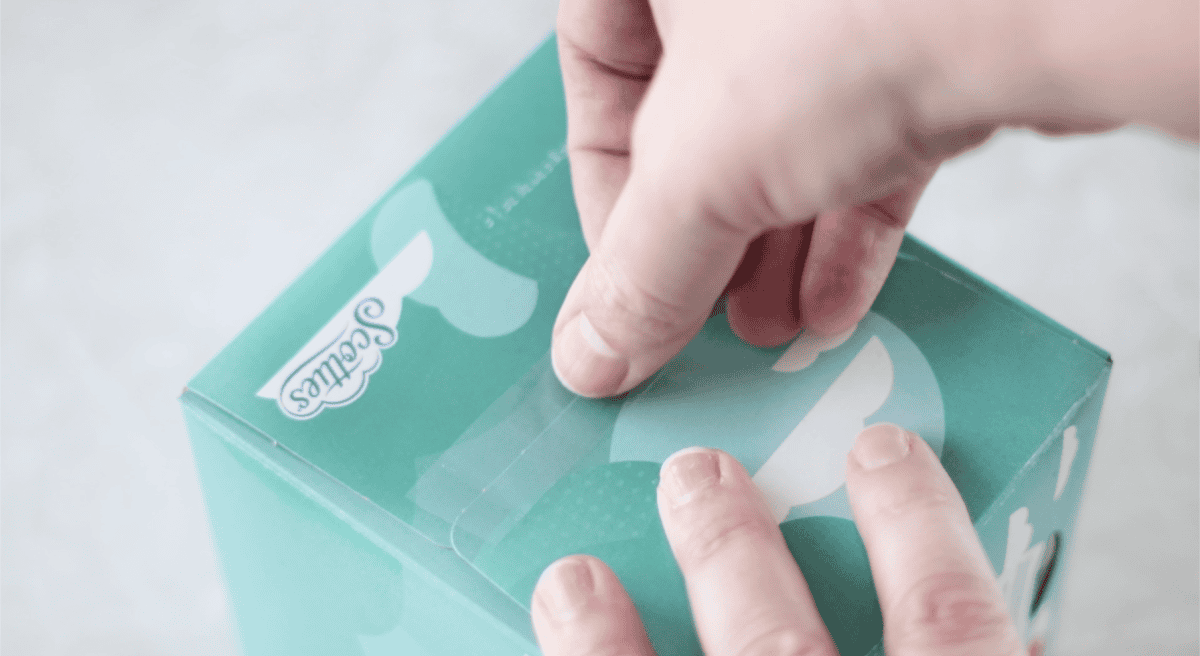 Hand taping side of tissue box closed.