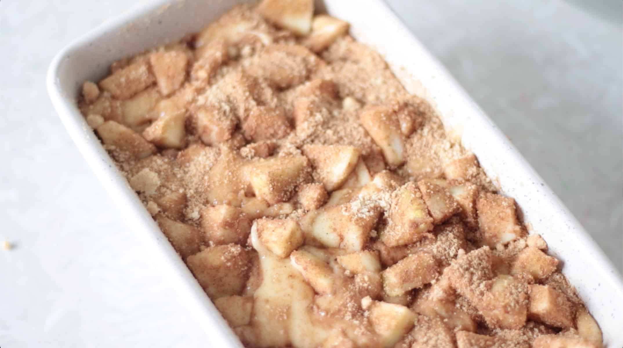 Loaf pan with apple fritter bread batter and chopped apples.