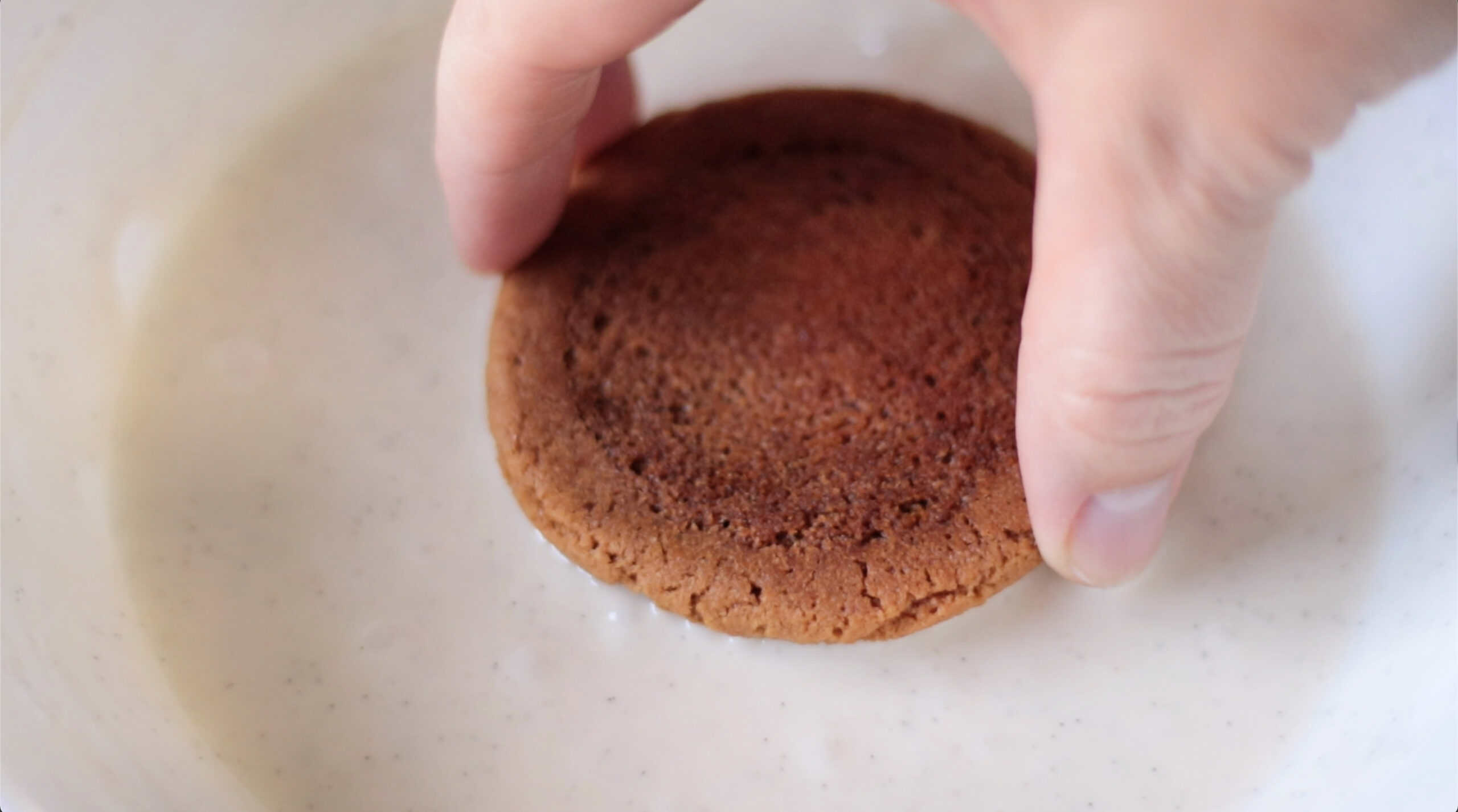 Hand dipping a molasses cookie in icing.