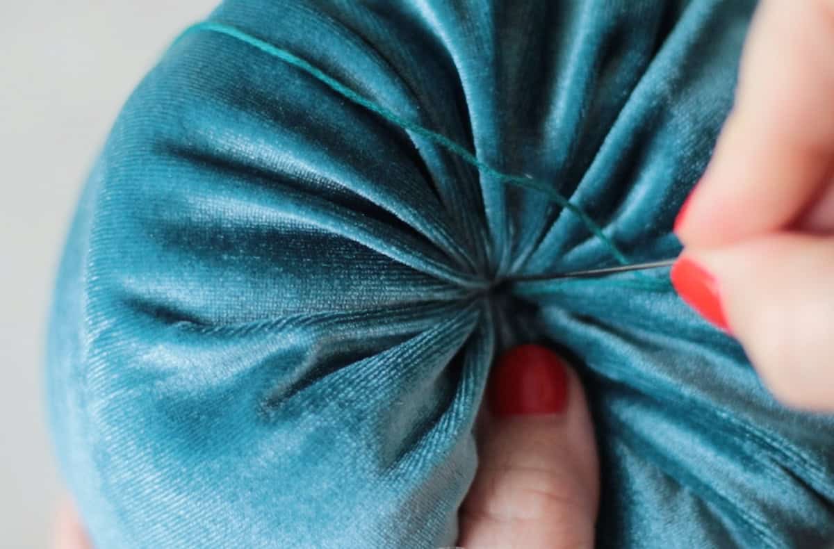 Hand poking needle through center of velvet pumpkin.