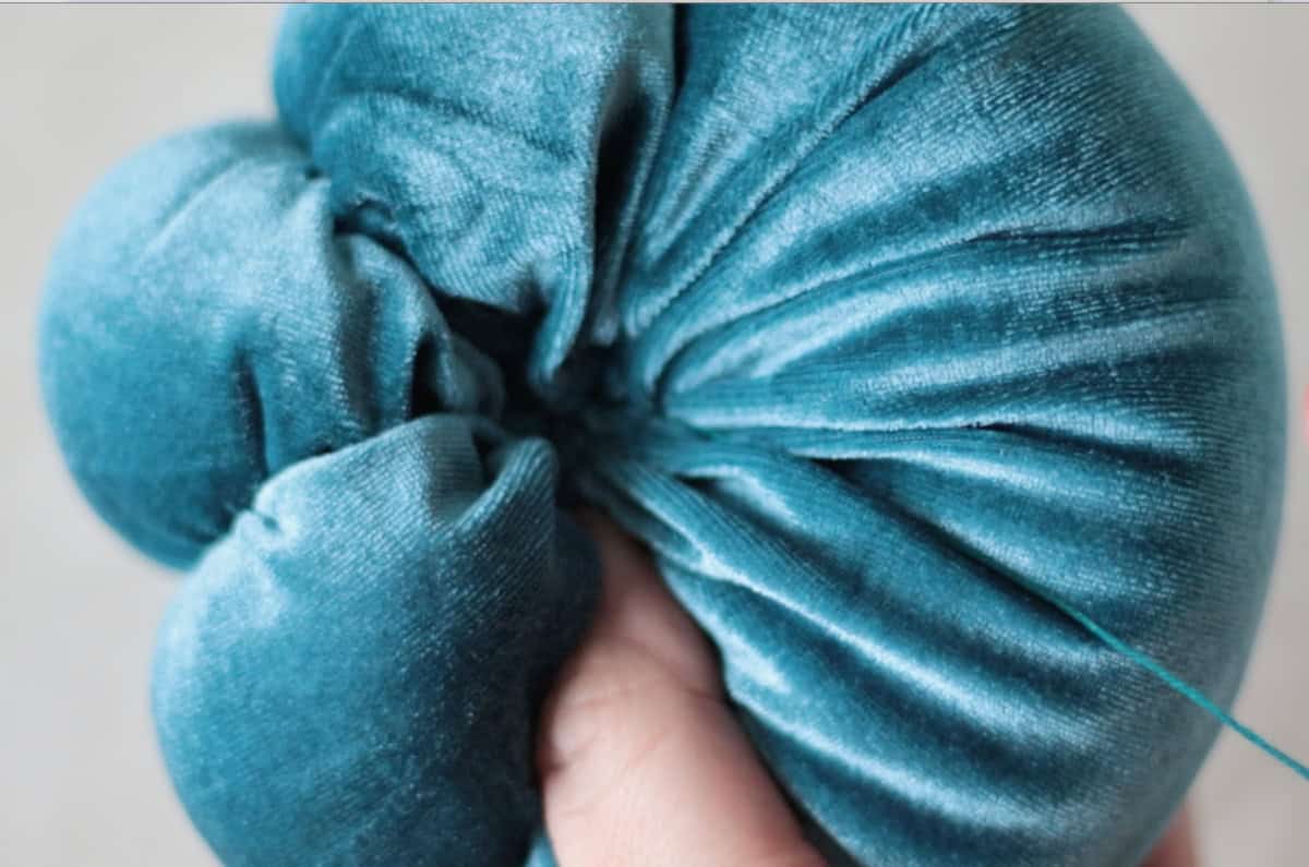 Hand holding velvet pumpkin and pulling string to create curves.