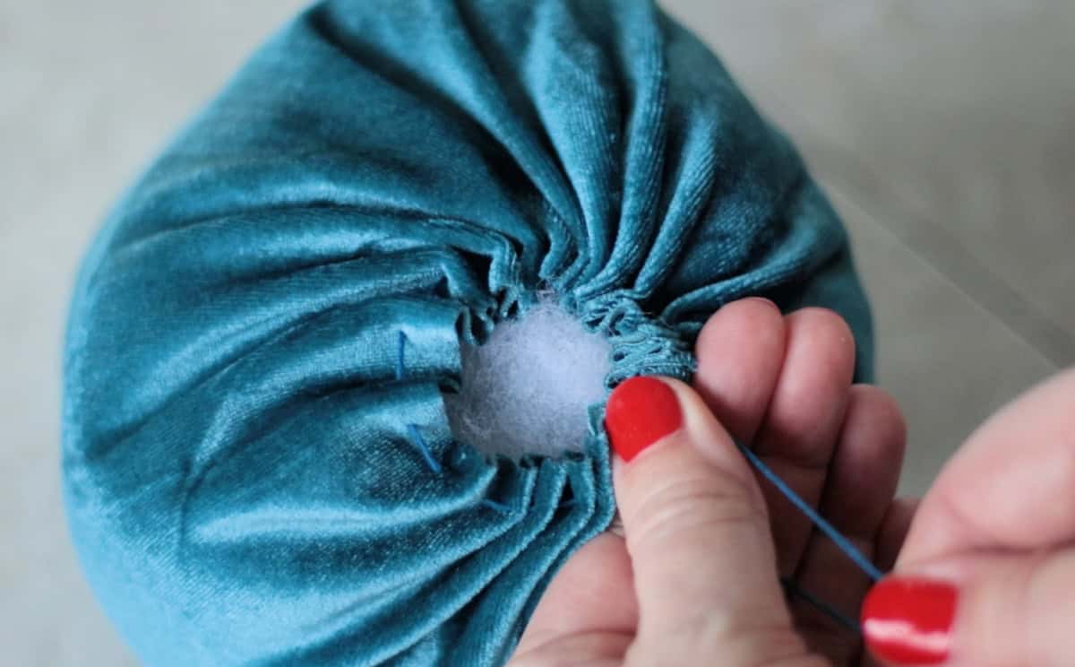 Hand pulling gathering strings on top of pumpkin.