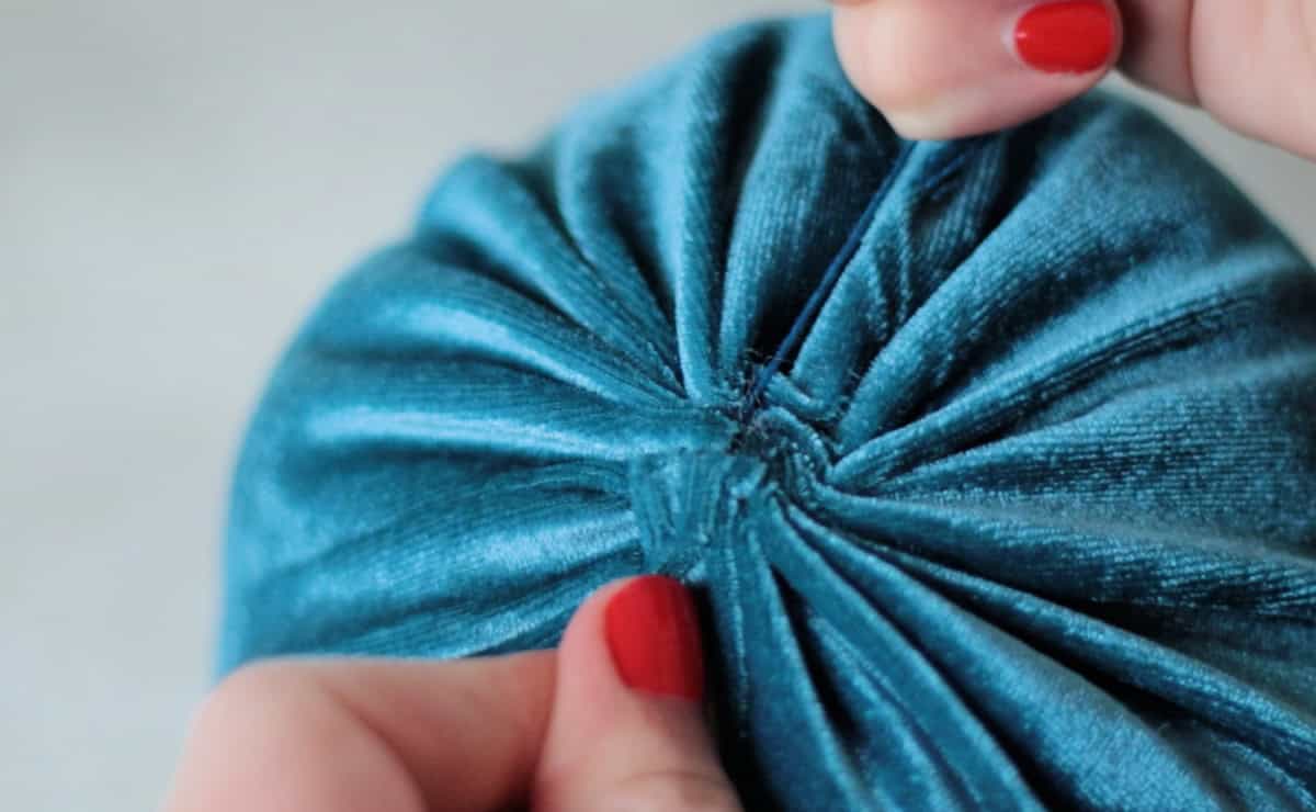 Hand pulling strings to tighten and close the top of the pumpkin.