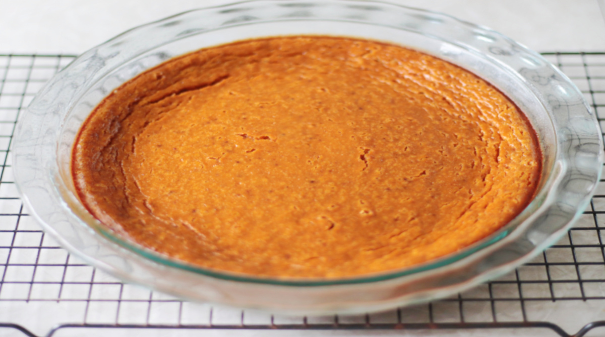 Pumpkin pie in pie dish cooling on wire rack.