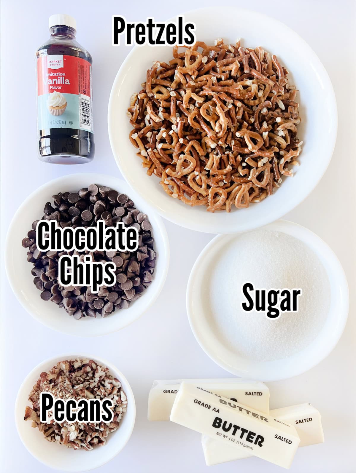 Bottle of vanilla, bowls of pretzels, chocolate chips, sugar, pecans and 3 sticks of butter.