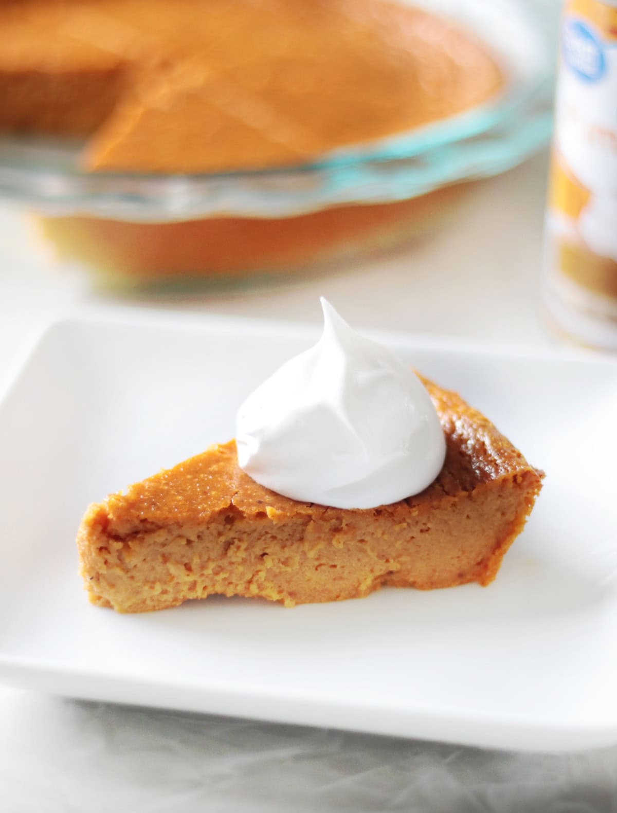 Slice of pumpkin pie on white plate with dollop of whipped cream.