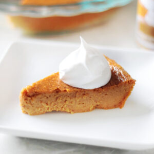 Slice of pumpkin pie with whipped cream on a white plate.