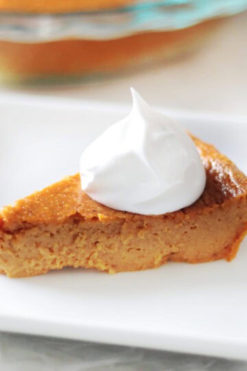 Slice of pumpkin pie with whipped cream on a white plate.