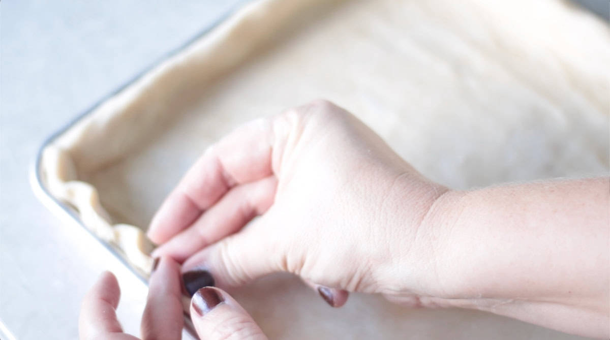 Hand crimping pie crust around the edge of the pie pan.
