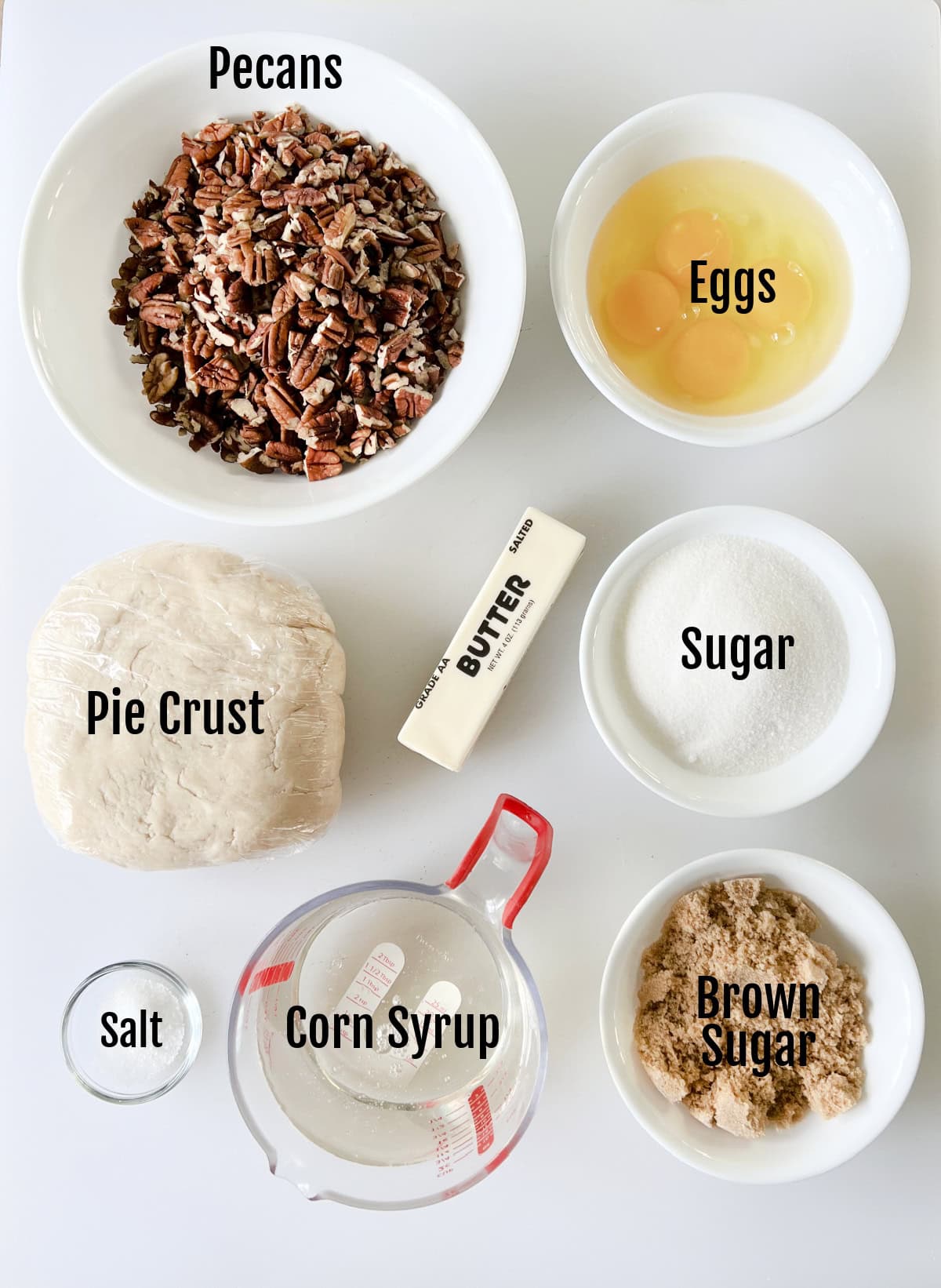 Bowls of pecan halves, eggs, stick of butter, sugar, brown sugar, salt, corn syrup and pie crust.
