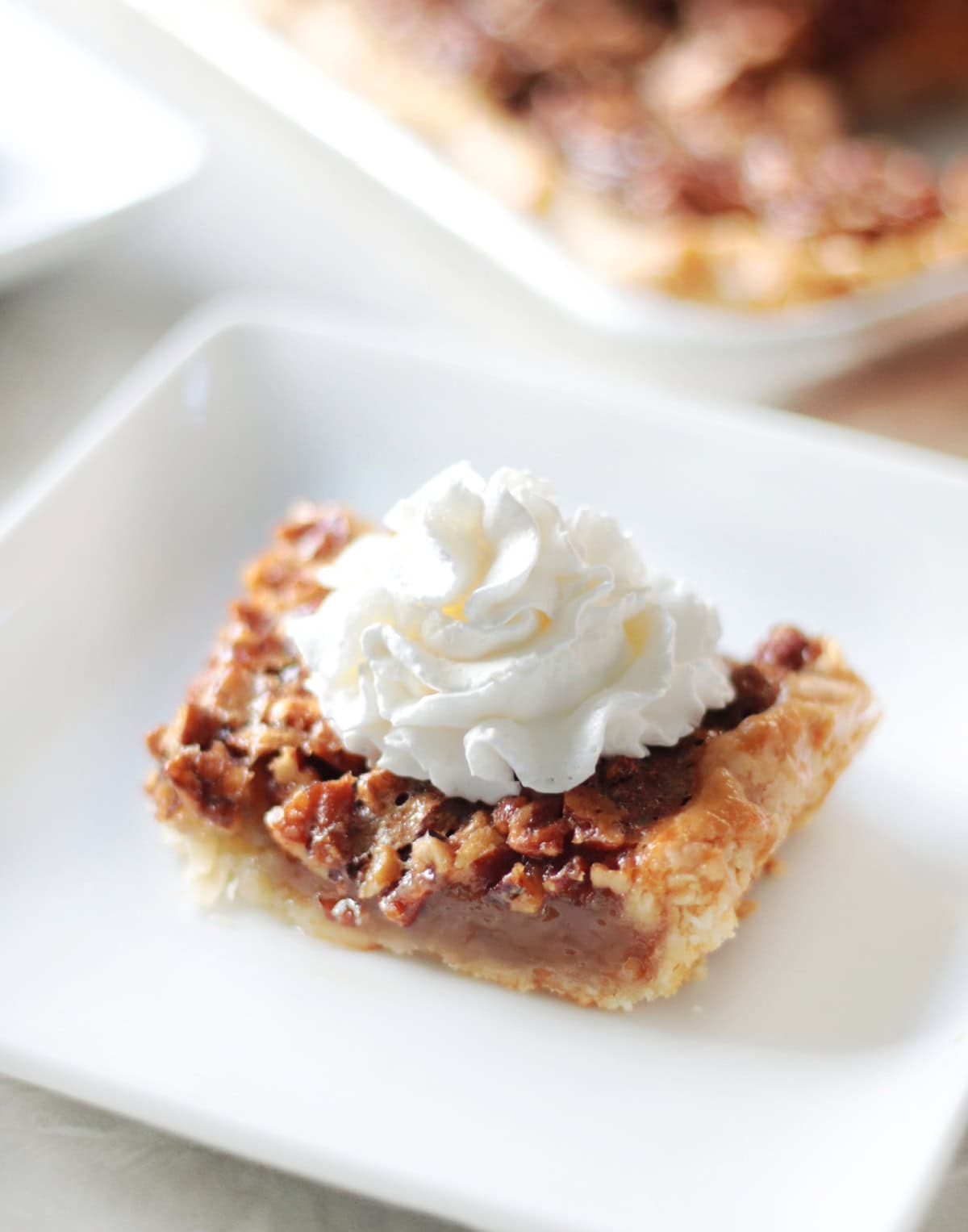 Slice of pecan slab pie with whipped cream on a white plate.
