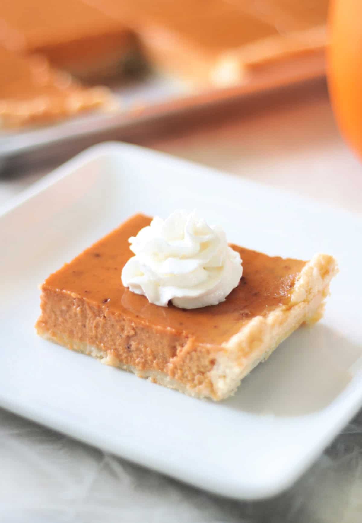 Slice of pumpkin slab pie on a white plate with whipped cream on top.