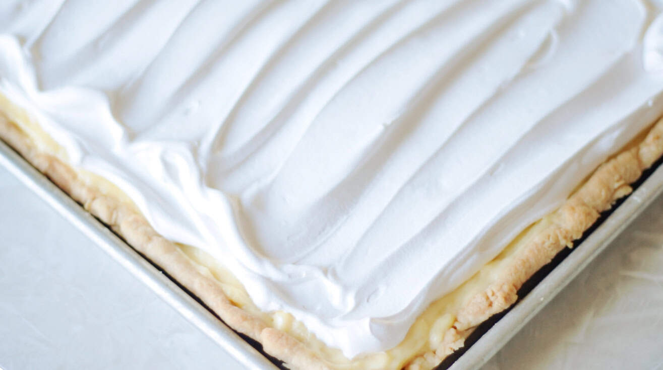 Jelly roll pan with baked pie crust, vanilla custard and whipped cream spread on top.