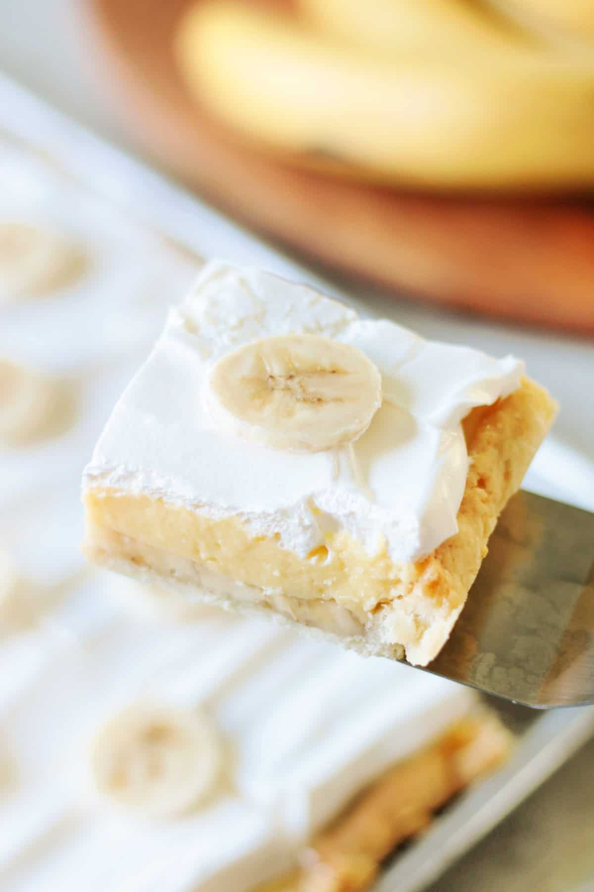 Slice of banana cream pie on a spatula.Everything you love about banana cream pie, baked in a sheet pan! One banana cream slab pie easily yields 18-24 slices.