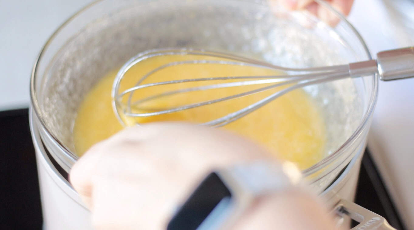 Hands placing bowl of egg mixture on top of a double boiler.