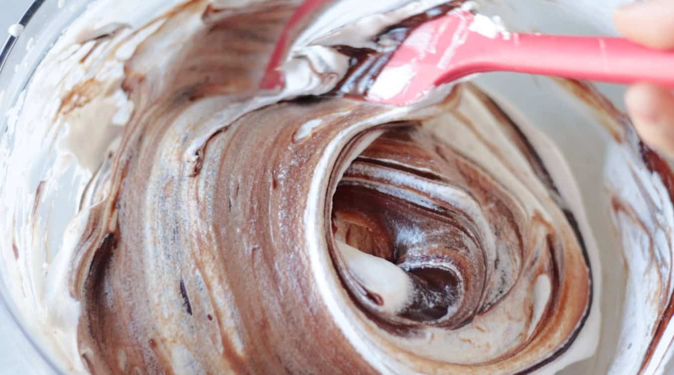 Red spatulat folding cream into chocolate mixture.