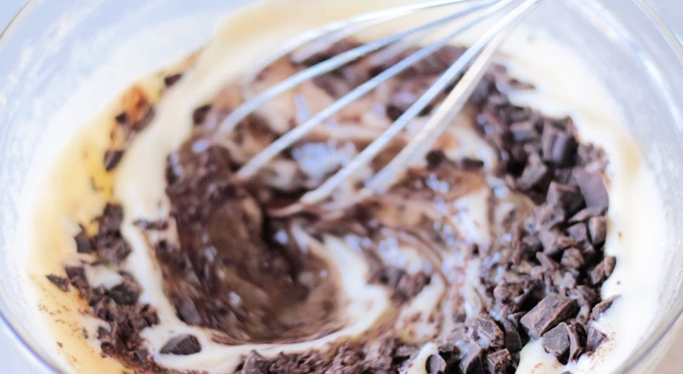 Bowl of egg mixture and chopped chocolate being mixed together.
