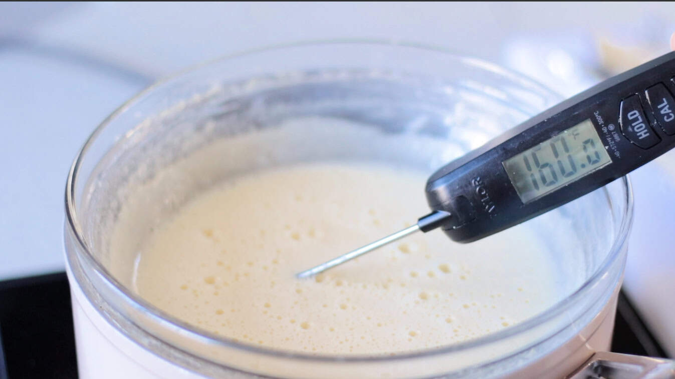 Digital thermometer inserted into bowl of egg and sugar mixture.