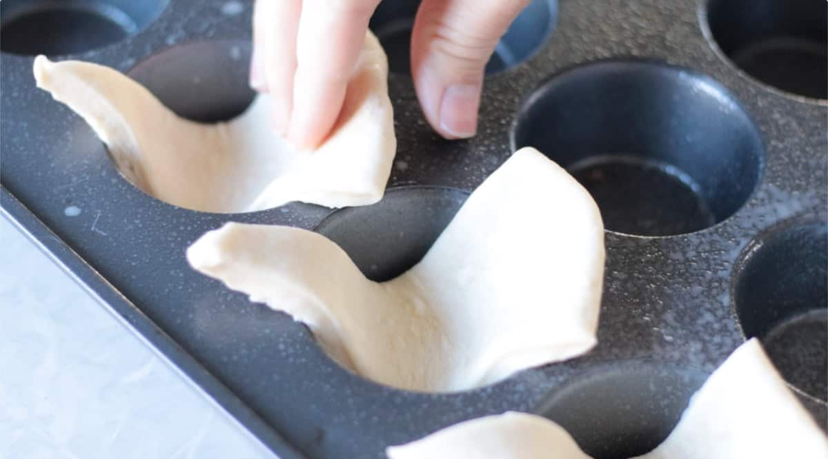 Muffin pan with triangles of roll dough placed inside.