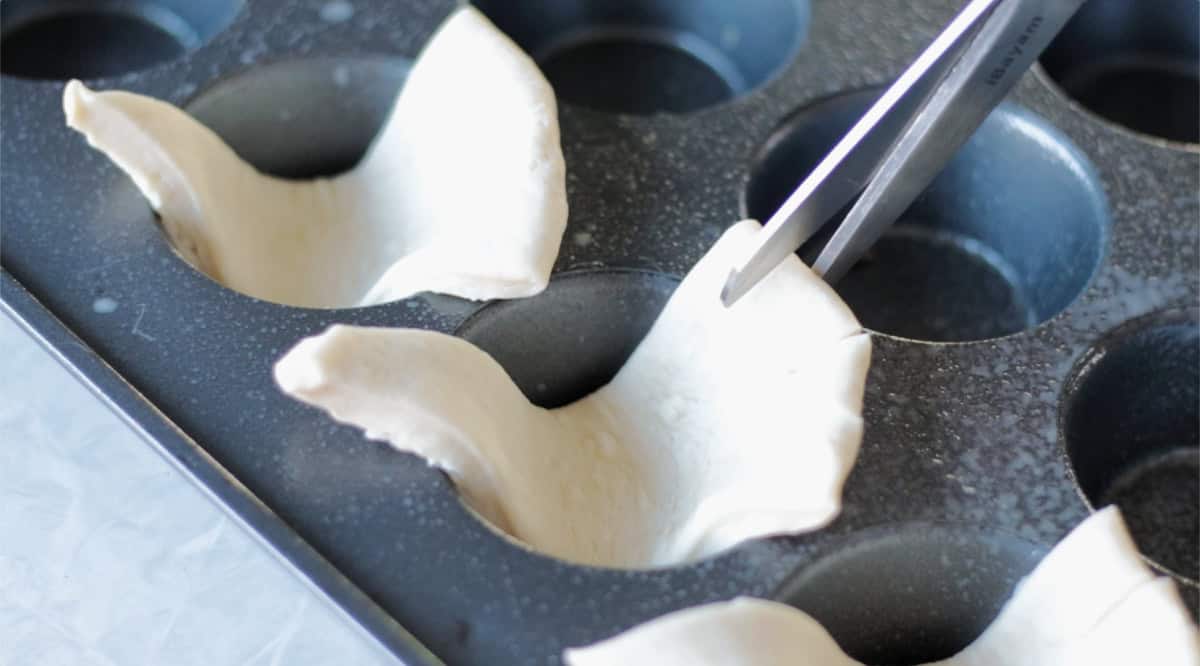 Turkey shaped rolls in muffin pan with scissors cutting slit for feathers.