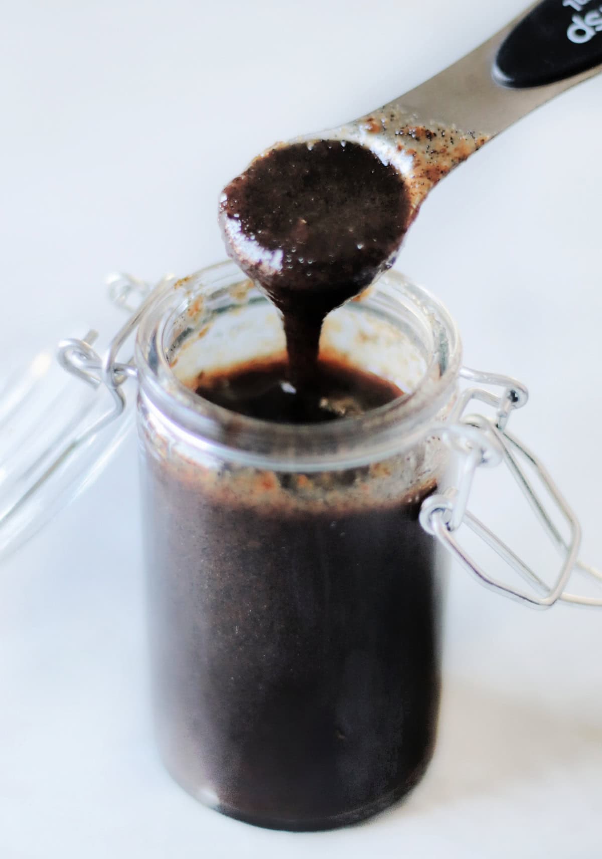 Spoon of vanilla paste dripping into bottle.