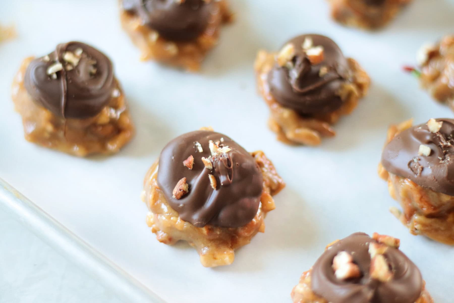 Peanut butter pretzel clusters on baking sheet with parchment paper and topped with chocolate and pecans.