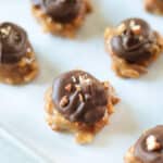 Peanut butter pretzel clusters on baking sheet with parchment paper and topped with chocolate and pecans.