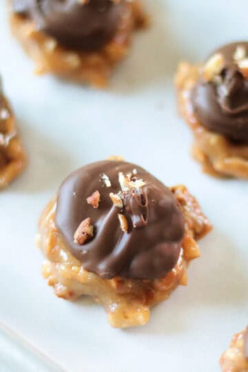 Peanut butter pretzel clusters on baking sheet with parchment paper and topped with chocolate and pecans.
