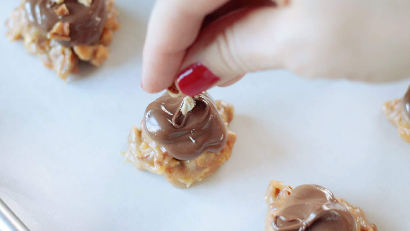 Hand adding chopped pretzels to the top of clusters.