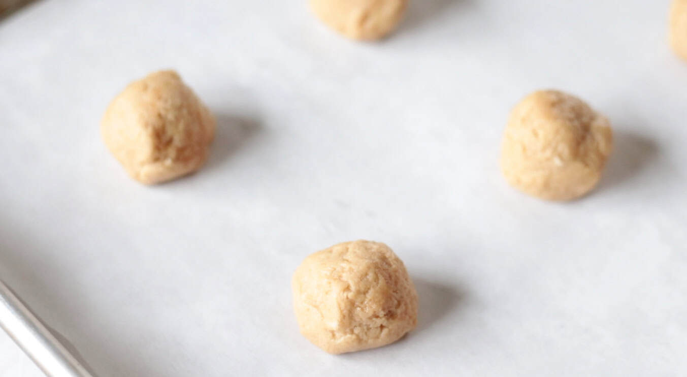Balls of peanut butter cookie dough on baking sheet lined with parchment paper.