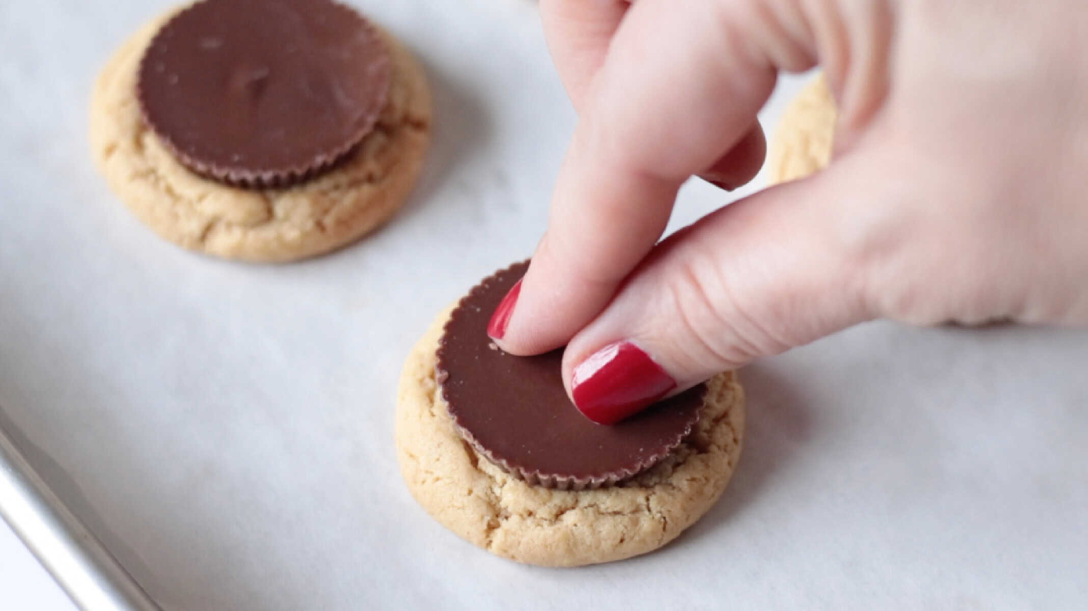 Hand pressing peanut butter cup into baked cookie.