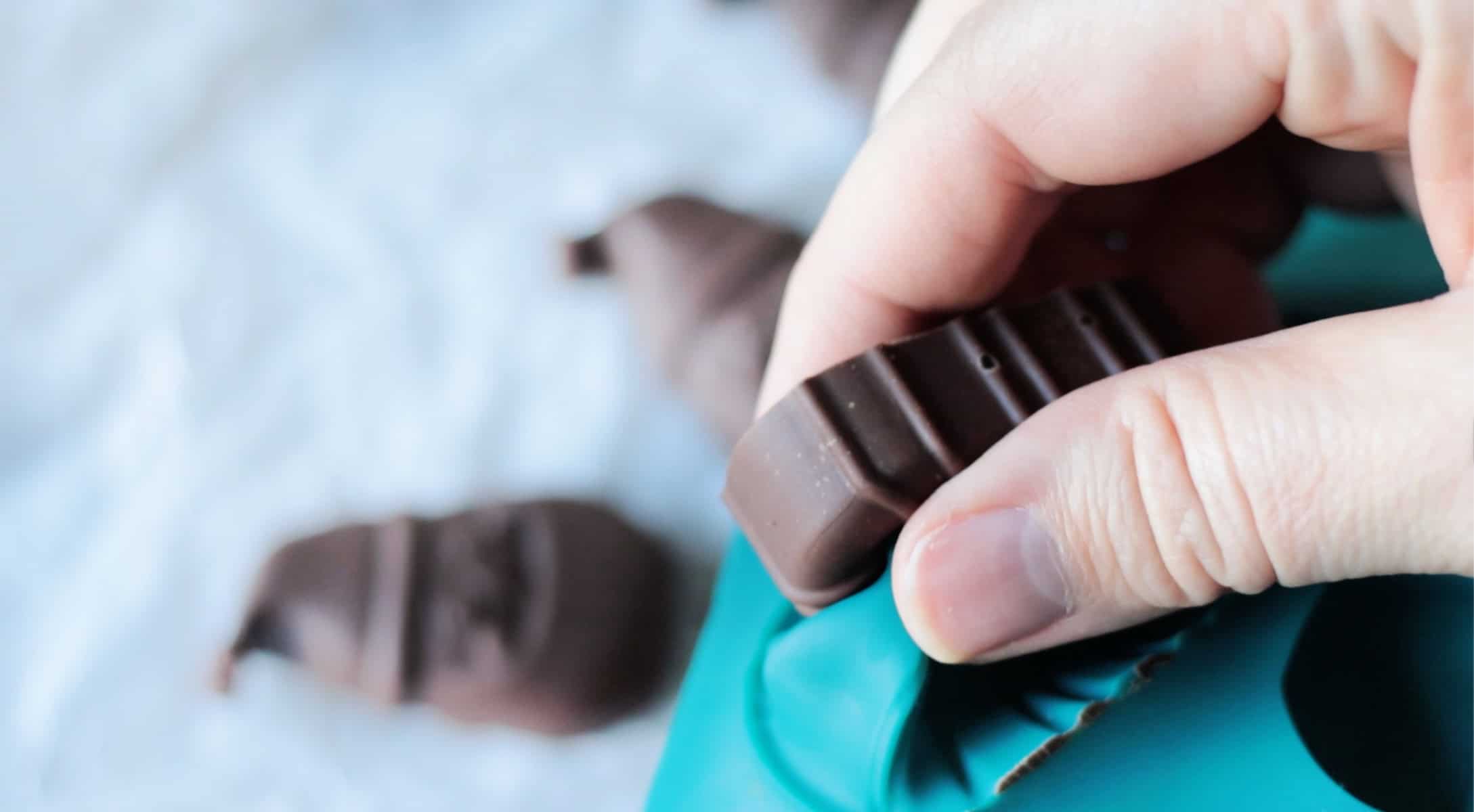 Hand removing hardened chocolate from candy mold.