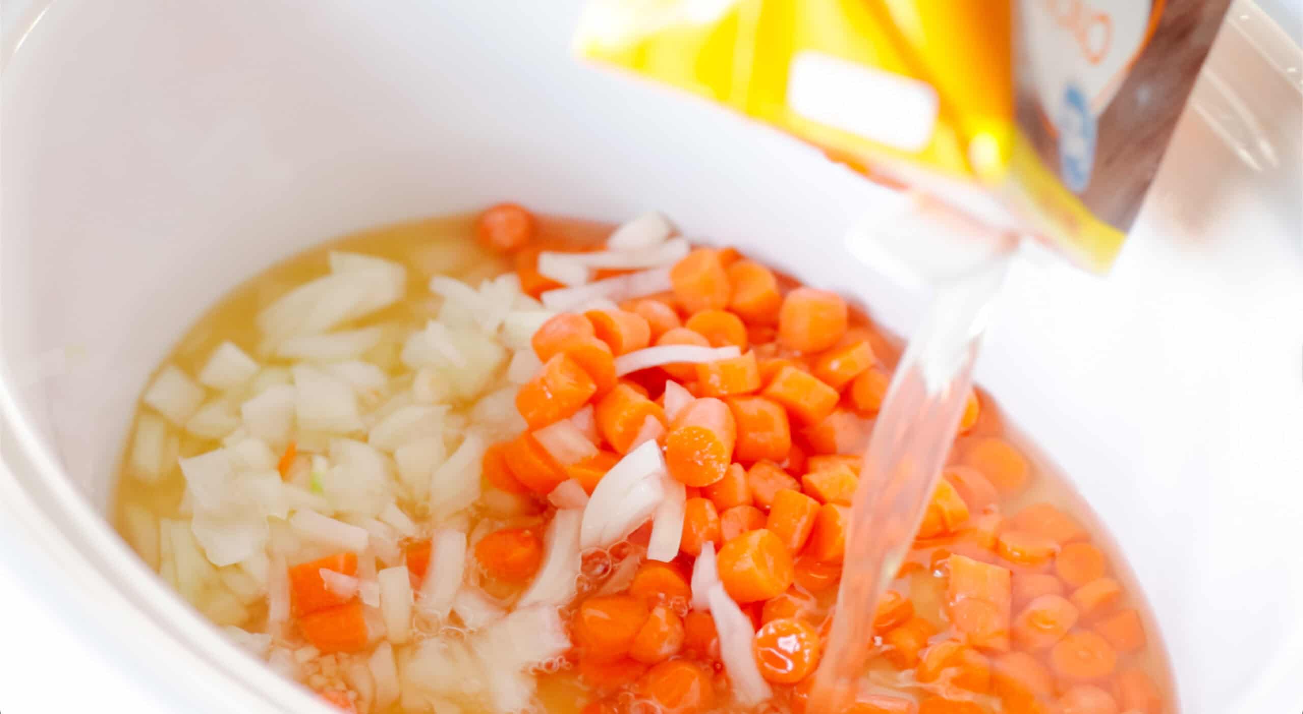 Slow cooker with diced carrots and onions.