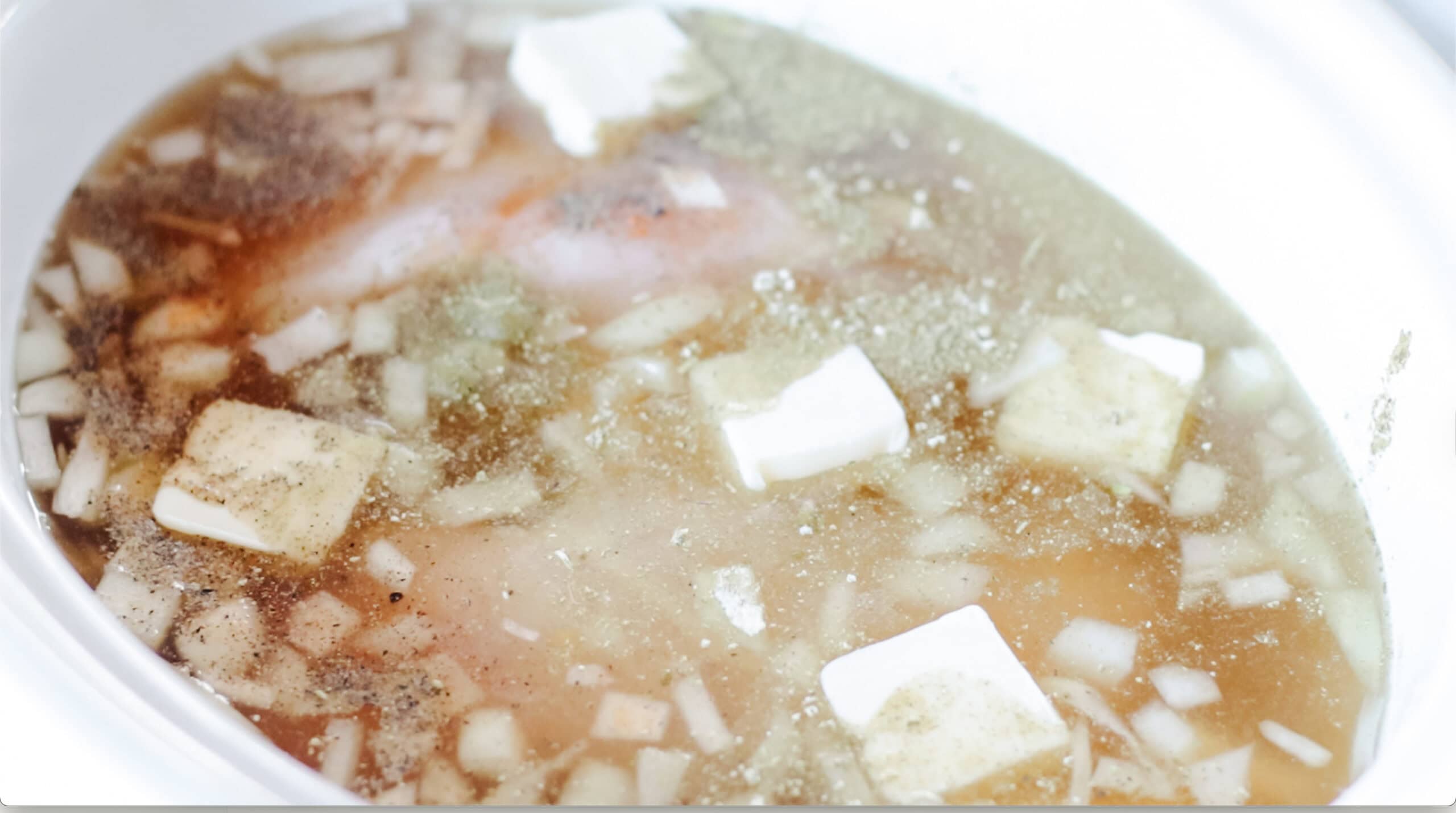 Slowcooker with broth, vegetables, chicken, and butter.