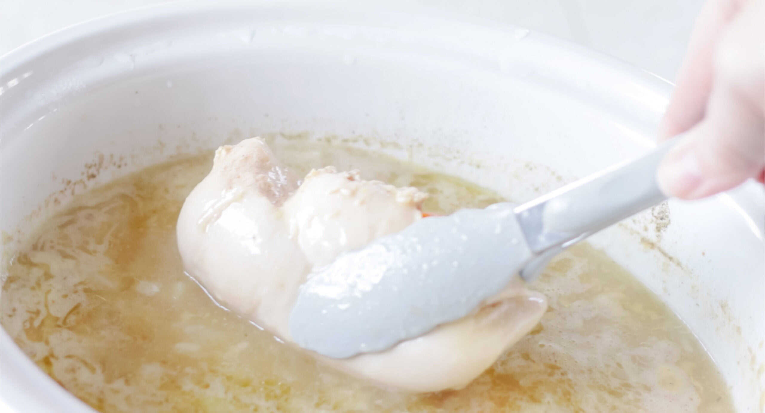 Slow cooker with cooked chicken breast in tongs.