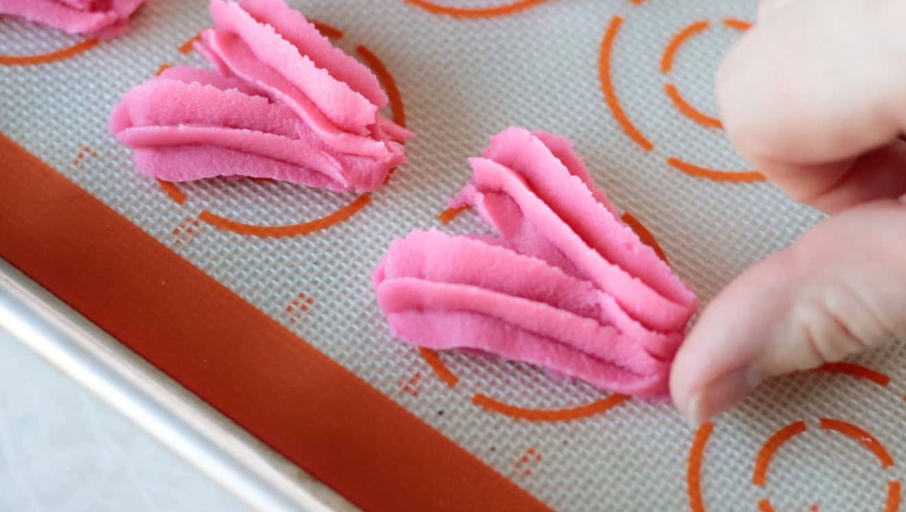 Fingers pinching off bottom of heart cookie.