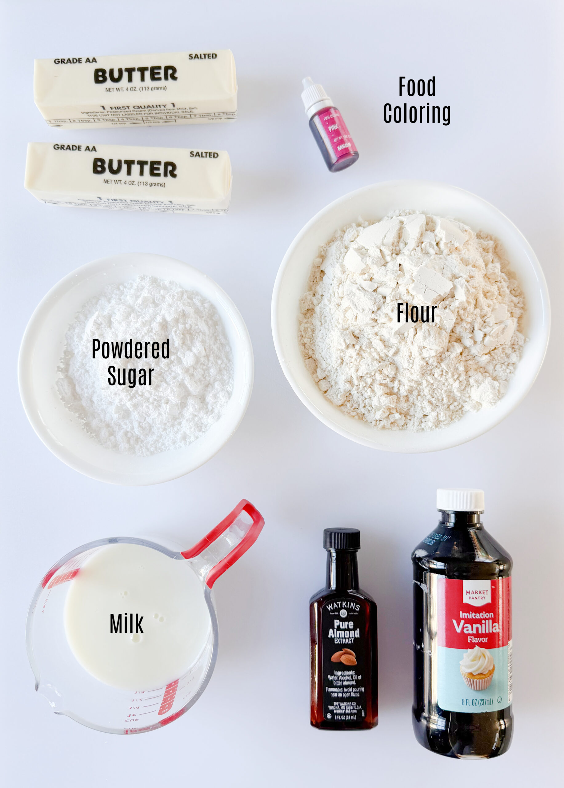 Bowls of flour and powdered sugar, bottles of vanilla extract and almond extract, cup of milk and two sticks of butter.