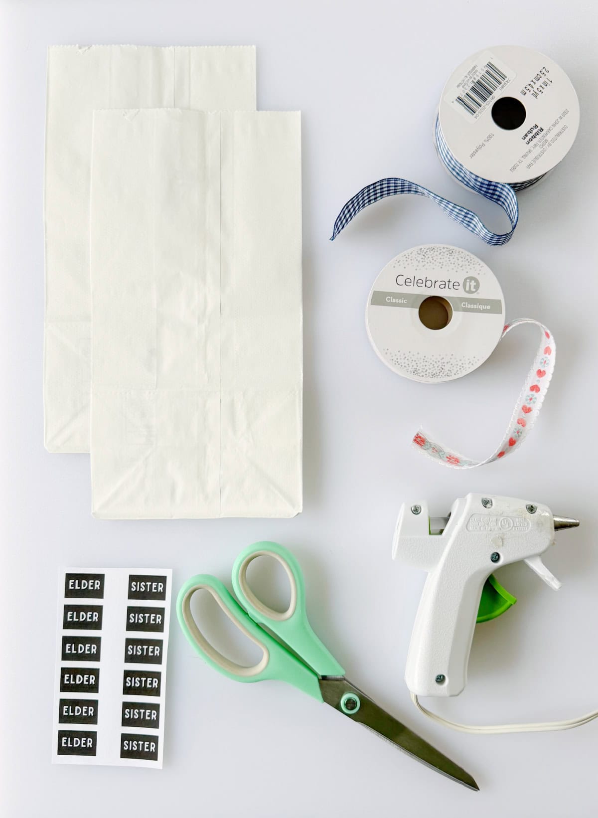 White paper bags, scissors, hot glue gun, two spools of ribbon and printable missionary name tags.
