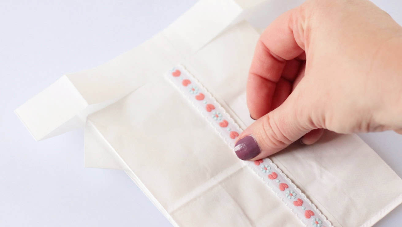 Hands gluing ribbon to front of white paper bag.