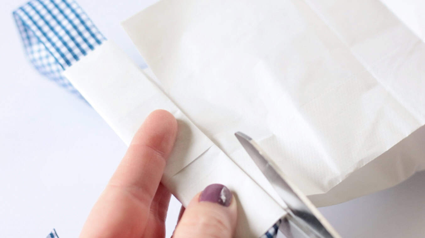 Scissors cutting slits into a white paper bag.