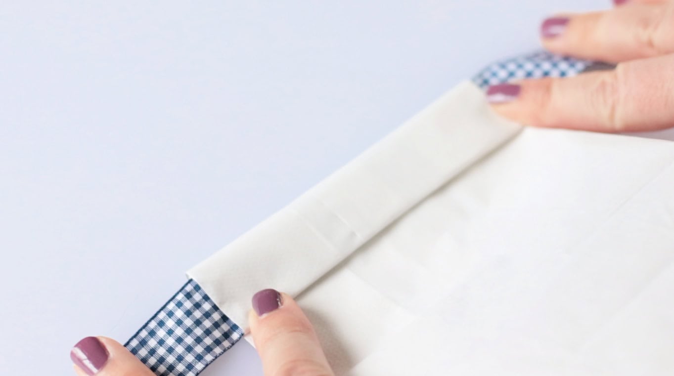 Top of white paper bag folded over ribbon.